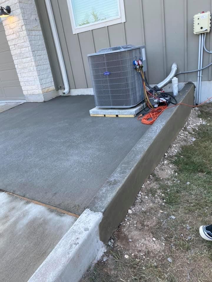 An air conditioner is sitting on top of a concrete driveway next to a house.