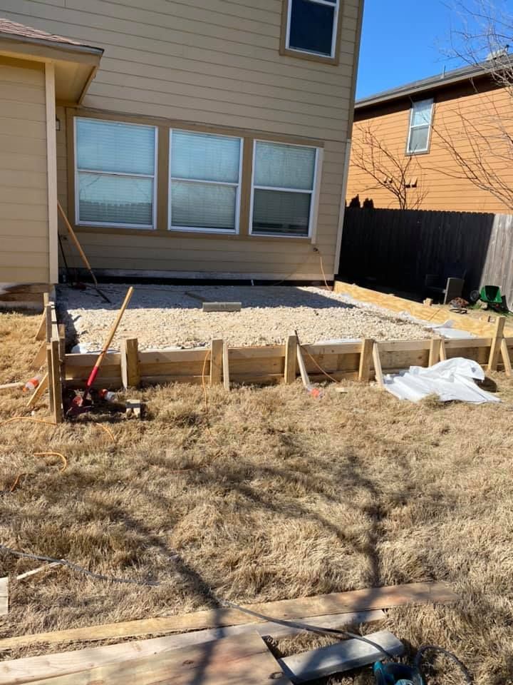 A concrete patio is being built in the backyard of a house.