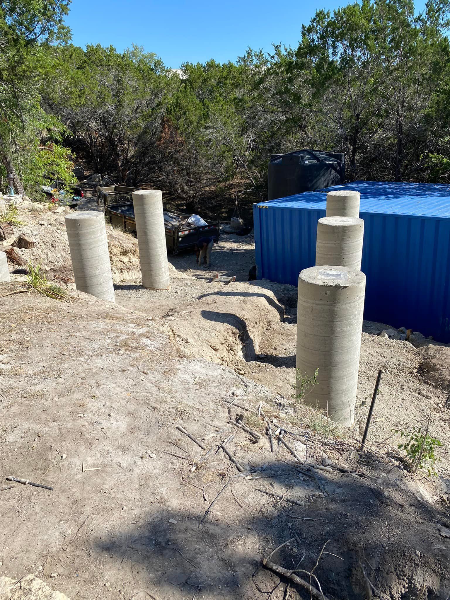 A group of concrete pillars are sitting in the dirt next to a blue tank.