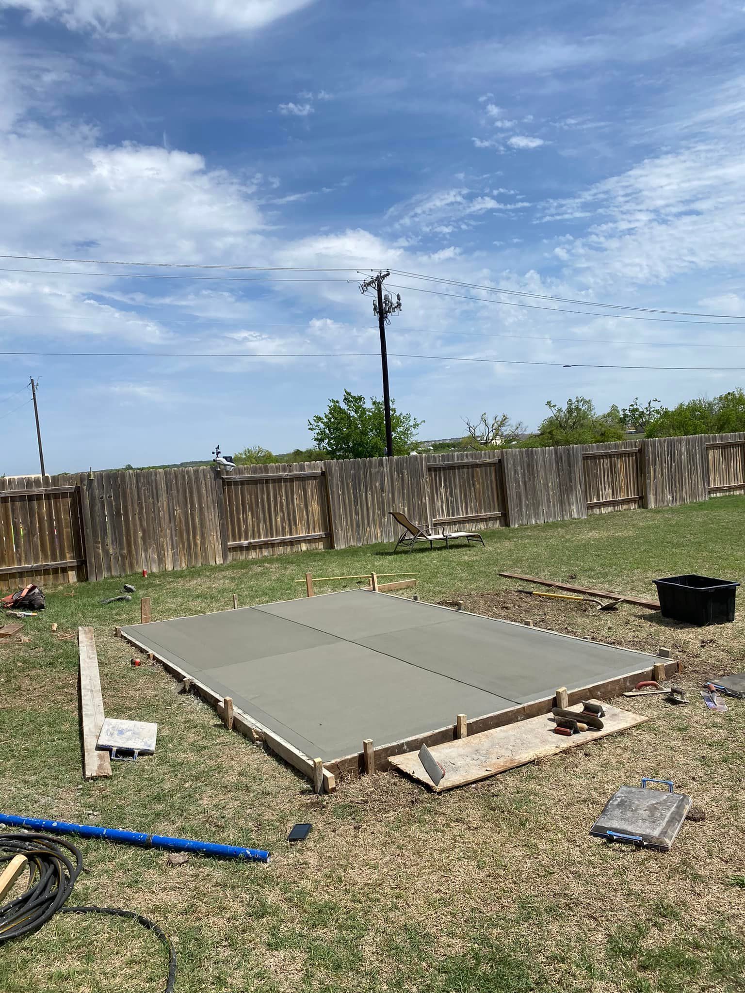 A concrete slab is being built in a backyard next to a wooden fence.