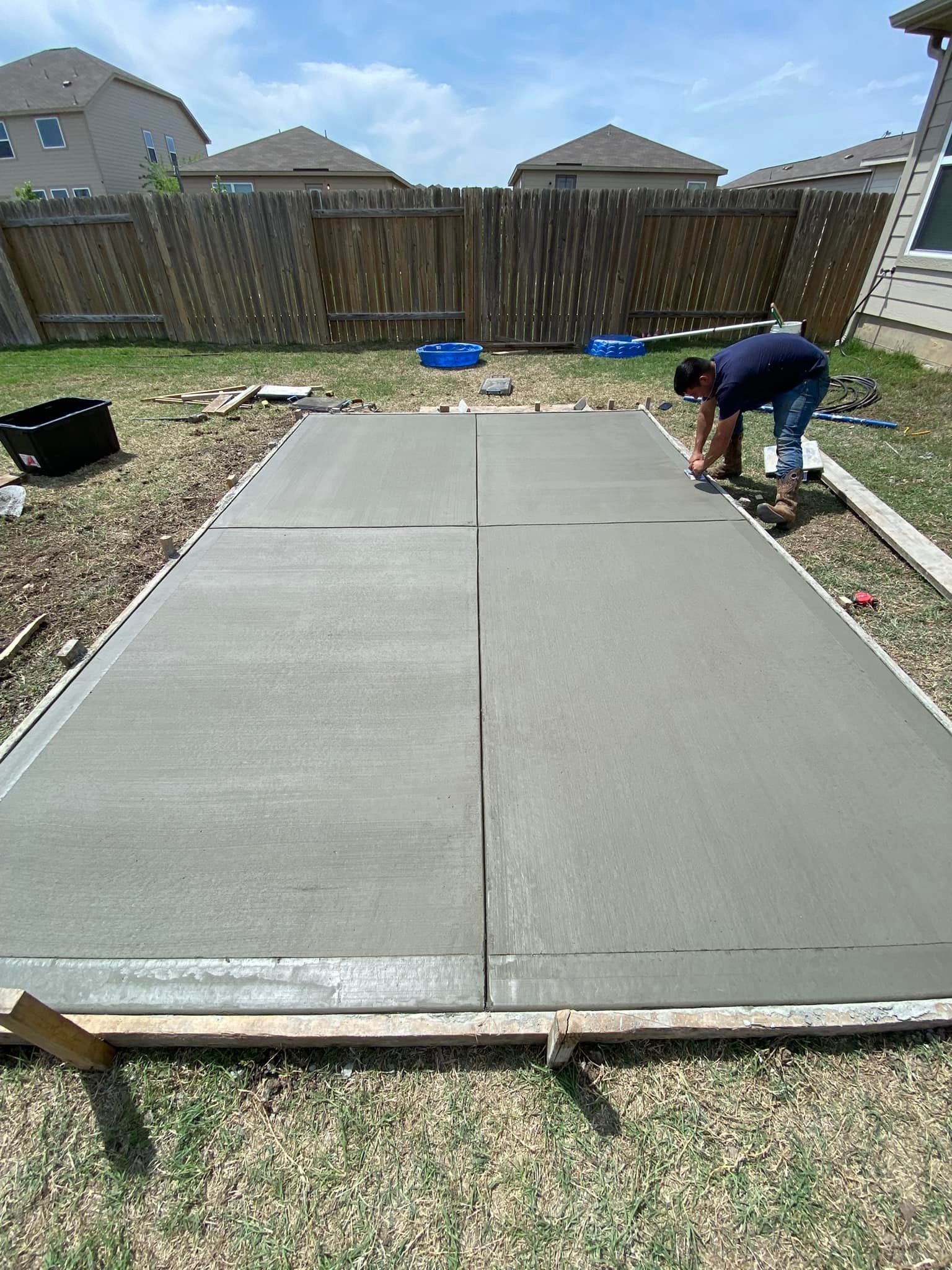 A man is working on a concrete driveway in a backyard.