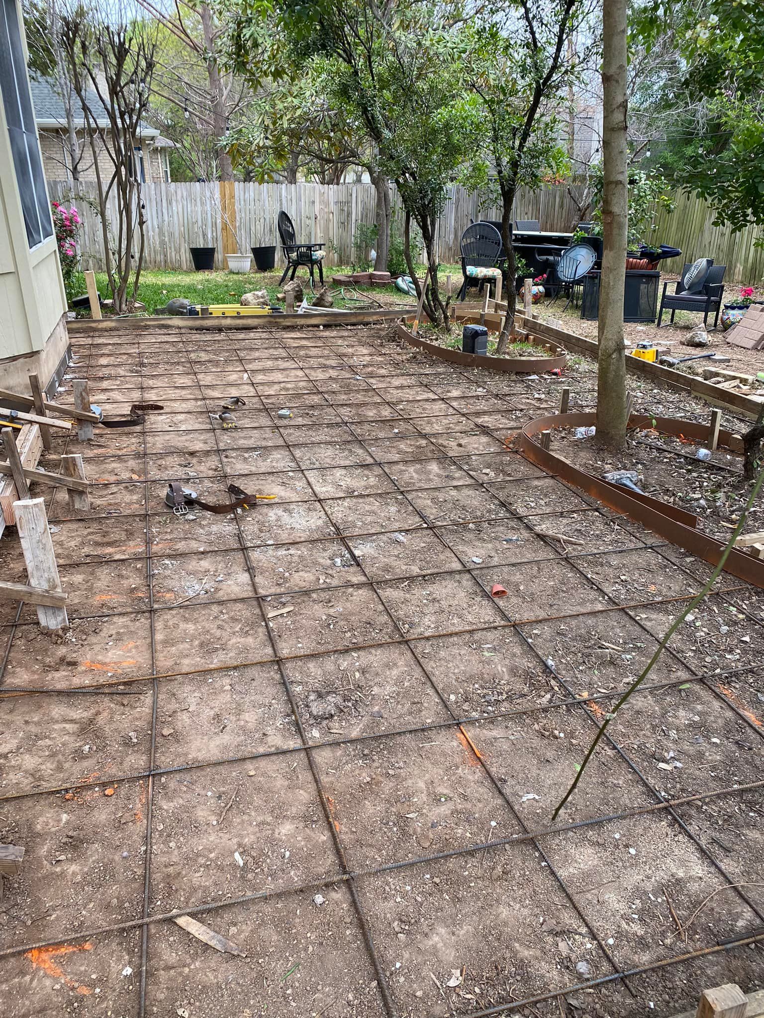 A concrete patio is being built in the backyard of a house.