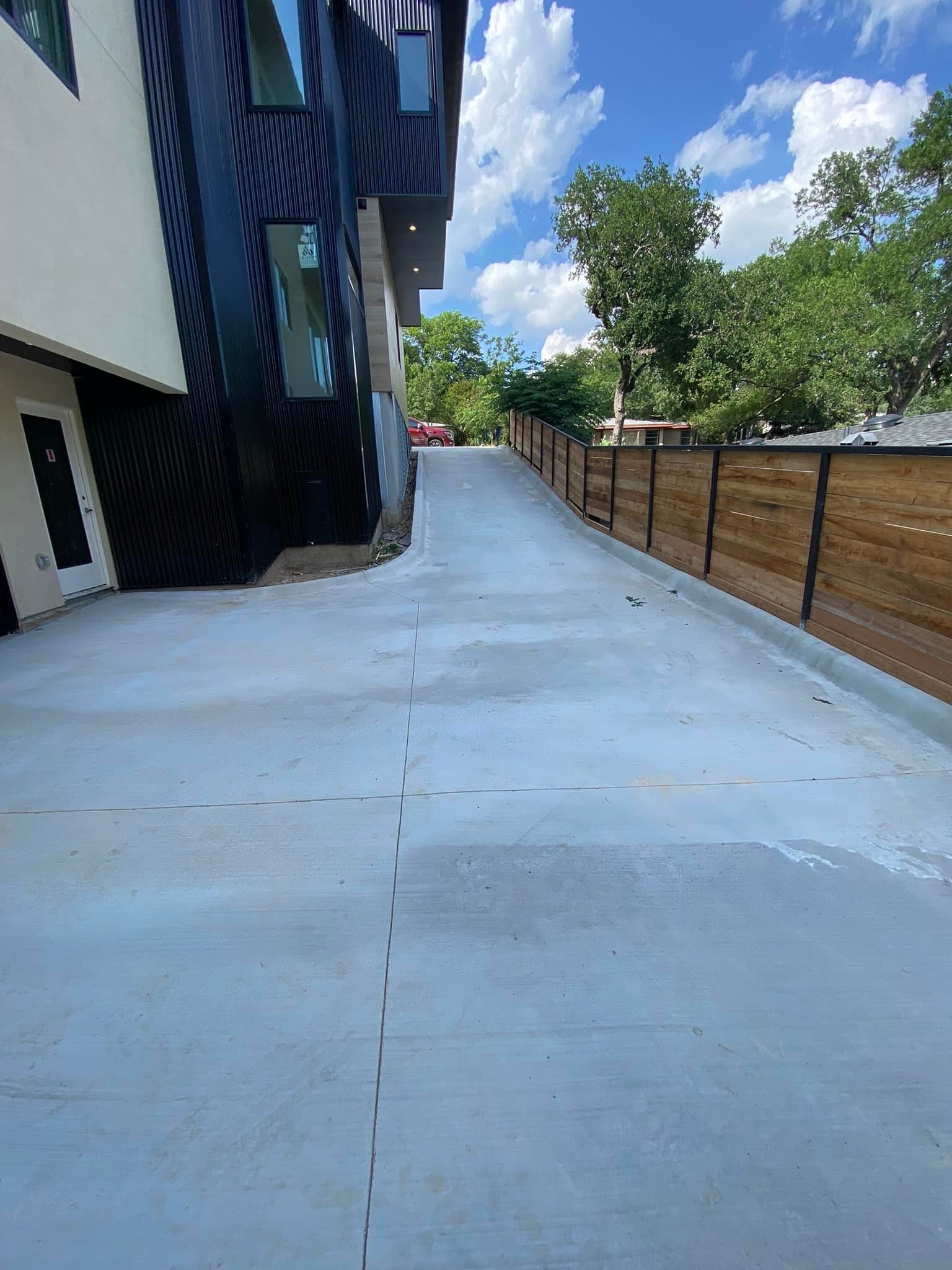 A concrete driveway leading to a building with a wooden fence.