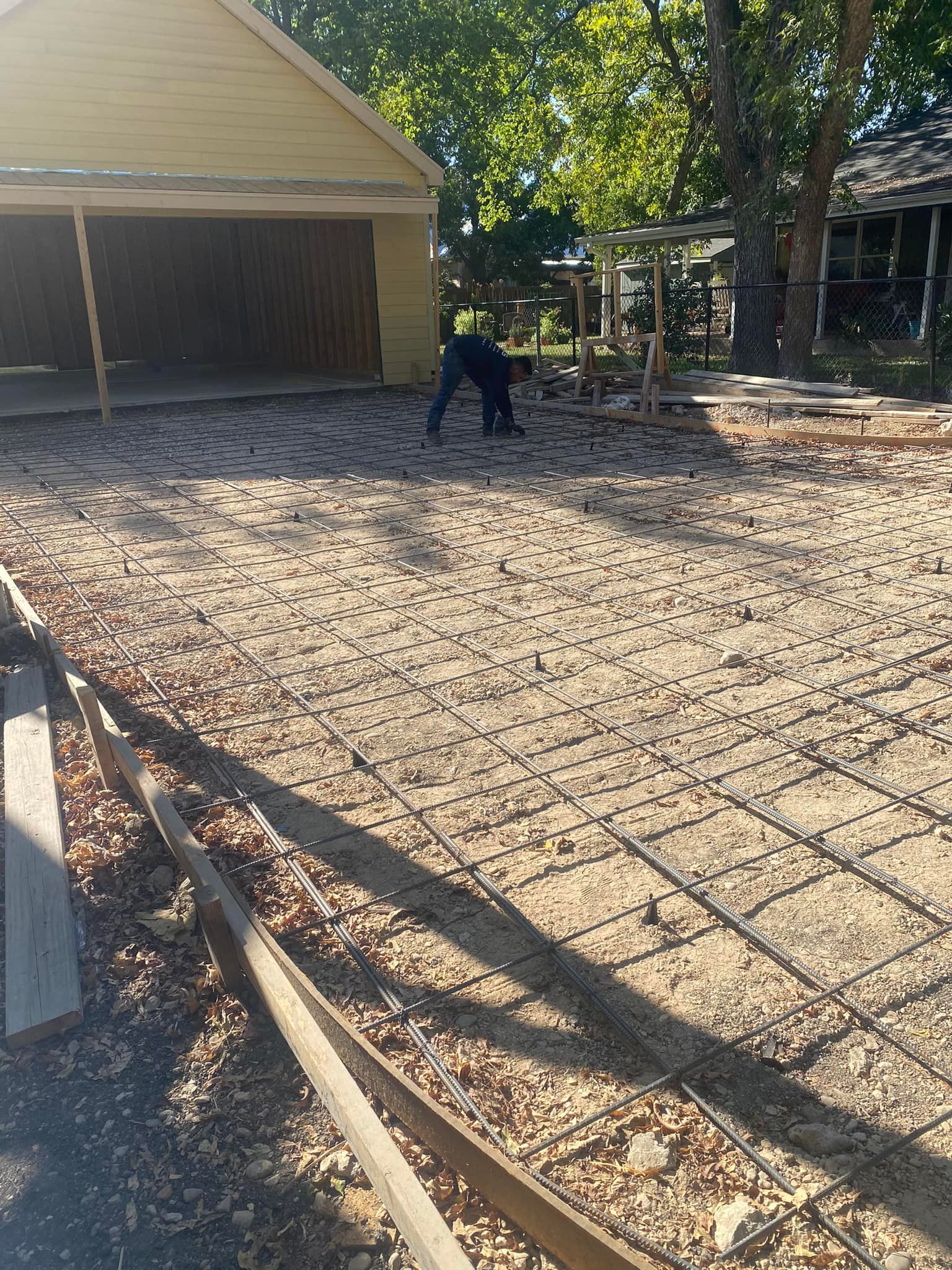 A man is laying concrete in a driveway in front of a garage.