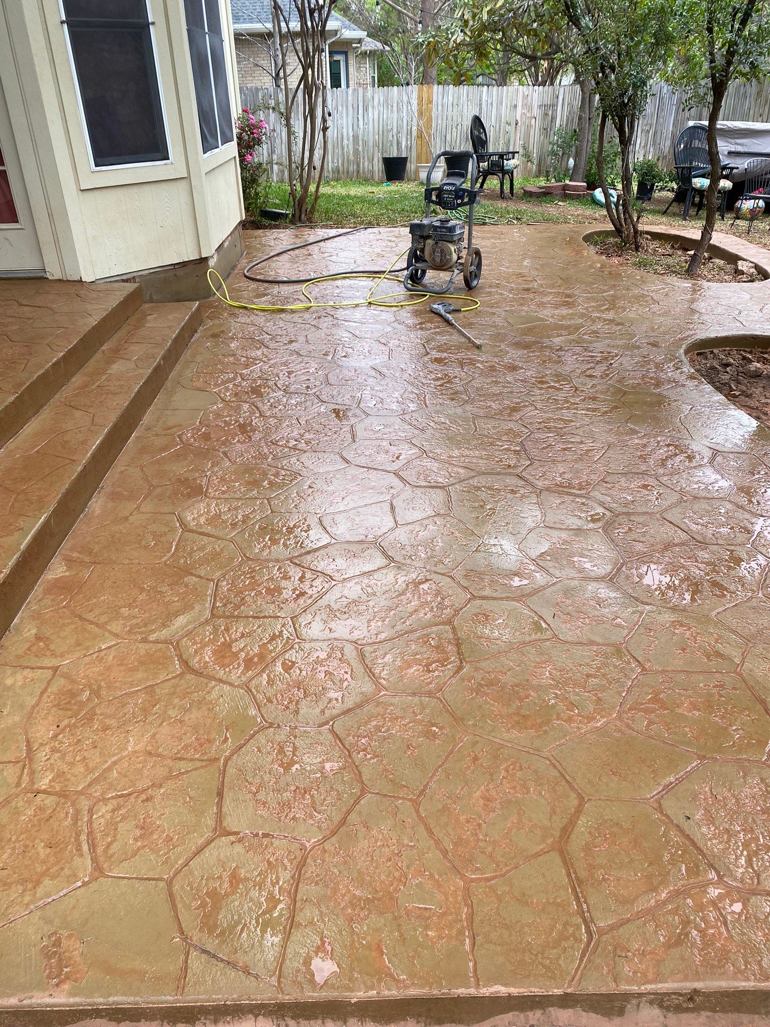 A pressure washer is cleaning a concrete patio in front of a house.