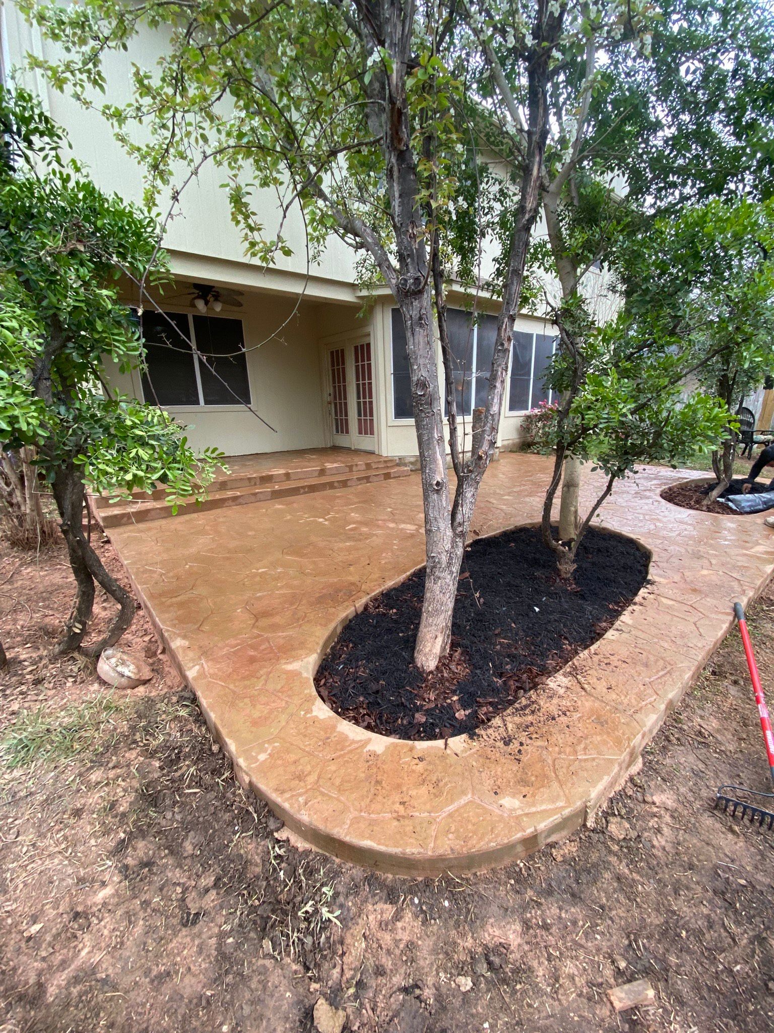 A concrete patio with a tree in the middle of it in front of a house.