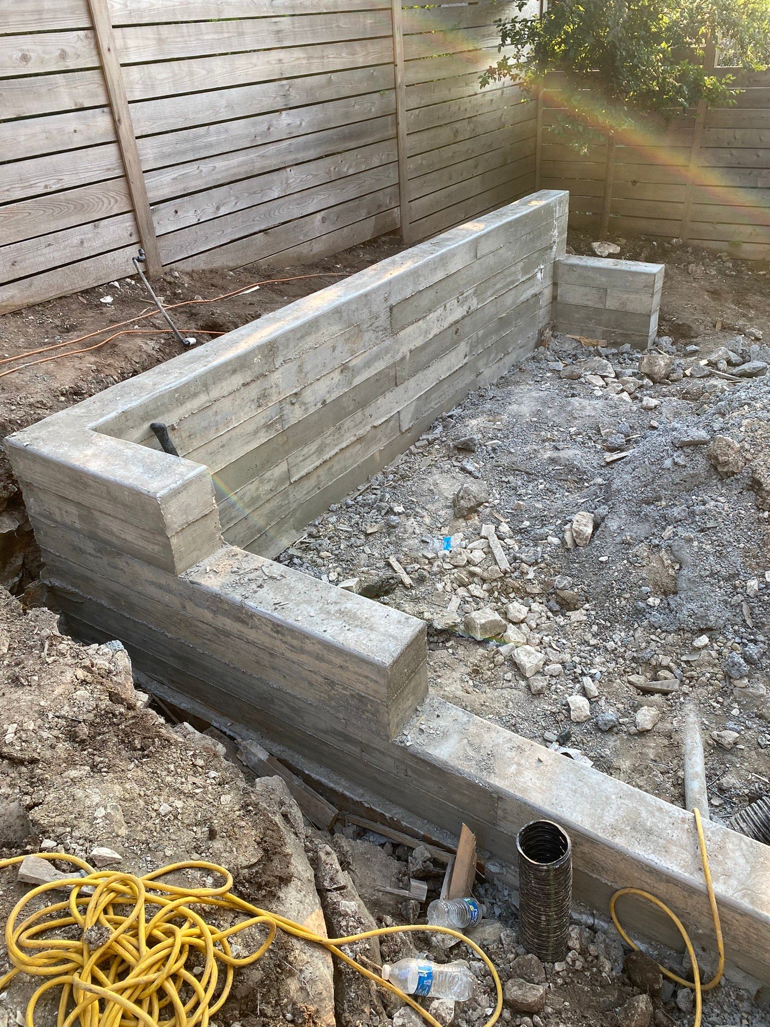 A concrete wall is being built in a backyard next to a wooden fence.