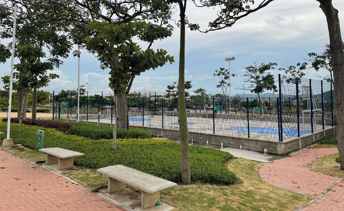 Un parque con bancos y árboles y una cancha de tenis al fondo.