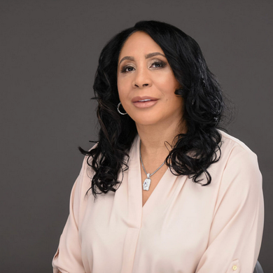 A woman with long black hair is wearing a necklace and earrings.