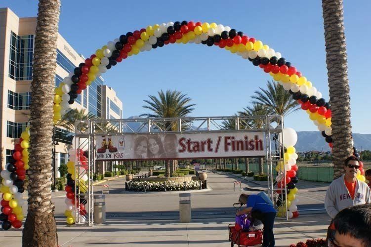 Start/Finish line arch with colorful balloons, event in front of a building with palm trees.