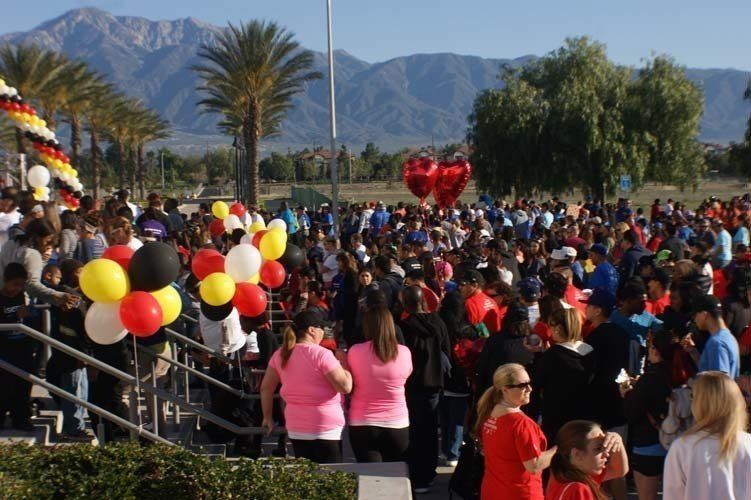Large crowd gathered outdoors with balloons, mountains in the background.