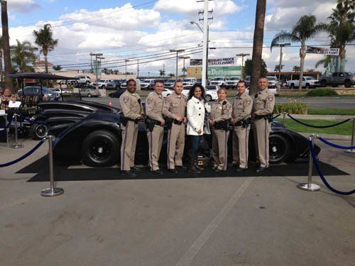 A woman and law enforcement officers stand with a black sports car outside a business.