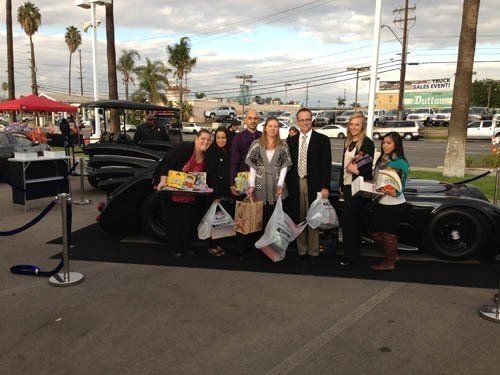 Group of people with shopping bags next to a black car at an outdoor event.