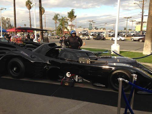 Batmobile parked on display with a person in a police uniform standing next to it.