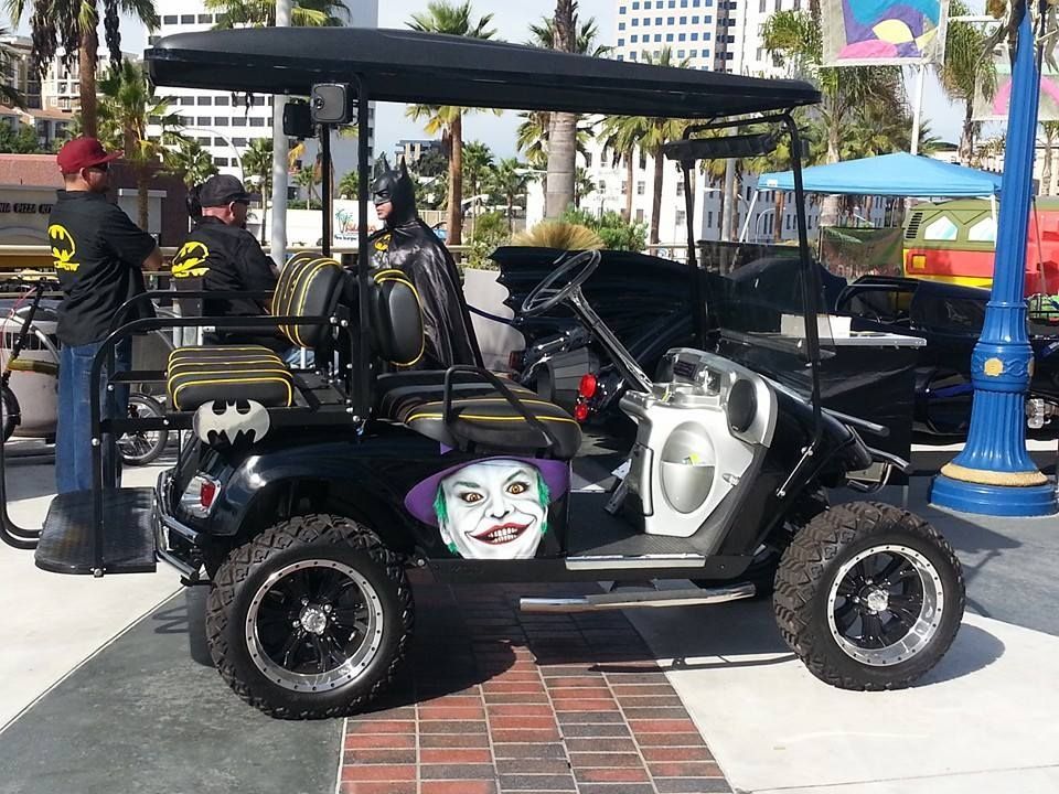 Batman-themed golf cart with a Joker graphic on the side, parked on a brick-paved area.