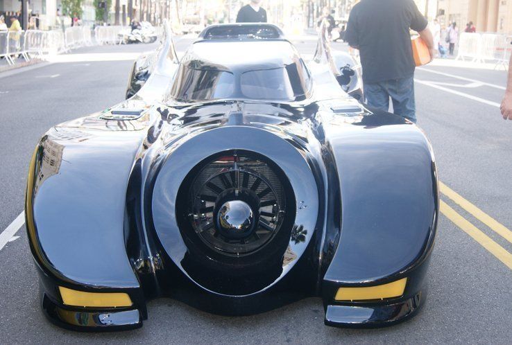 Black Batmobile on a city street, with a large central turbine and people in the background.