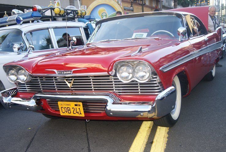 Red vintage Plymouth with white wall tires and chrome trim parked on a city street.