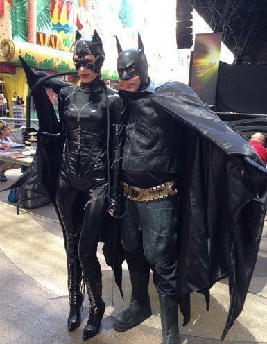 Catwoman and Batman cosplayers pose outdoors, both in black costumes.