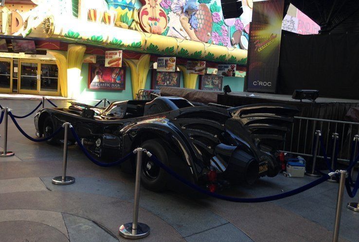 Batmobile on display outside a building, roped off with stanchions.