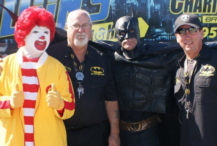 Ronald McDonald and Batman pose with two men; all smiling, thumbs up.