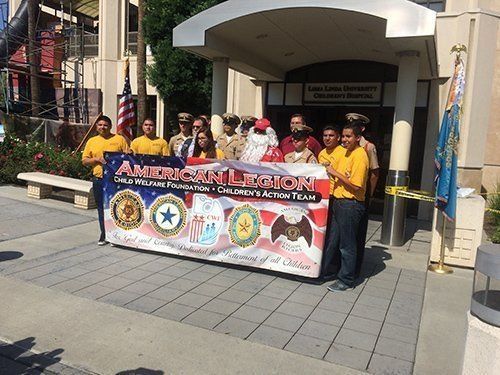 People holding a banner for American Legion Children’s Action Team in front of a building.