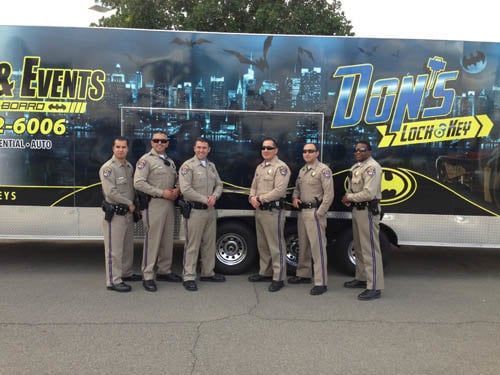 Six uniformed men stand in front of a van with a Batman-themed logo, possibly a locksmith service.