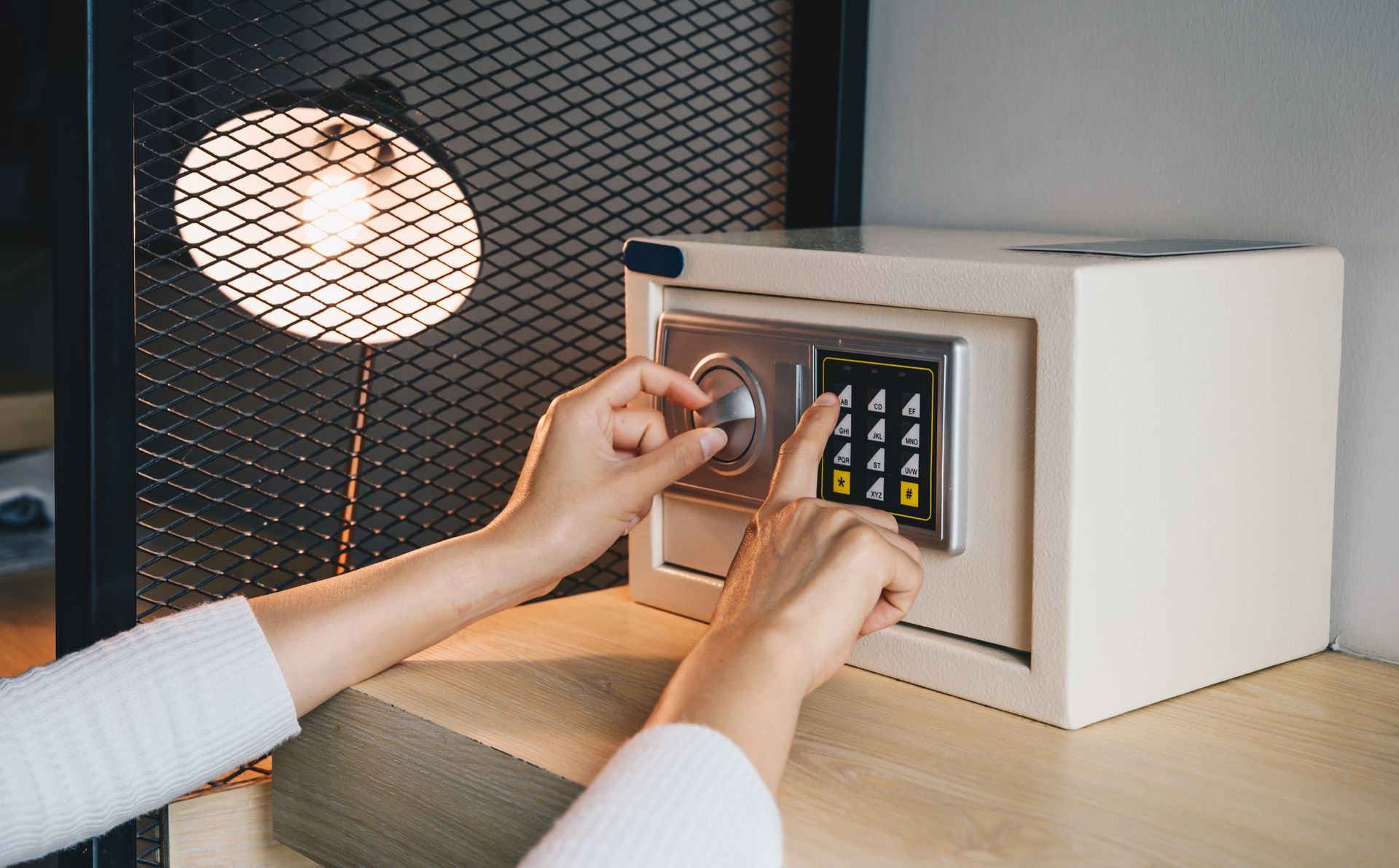 Hands opening a safe with a dial and keypad, illuminated by a lamp.