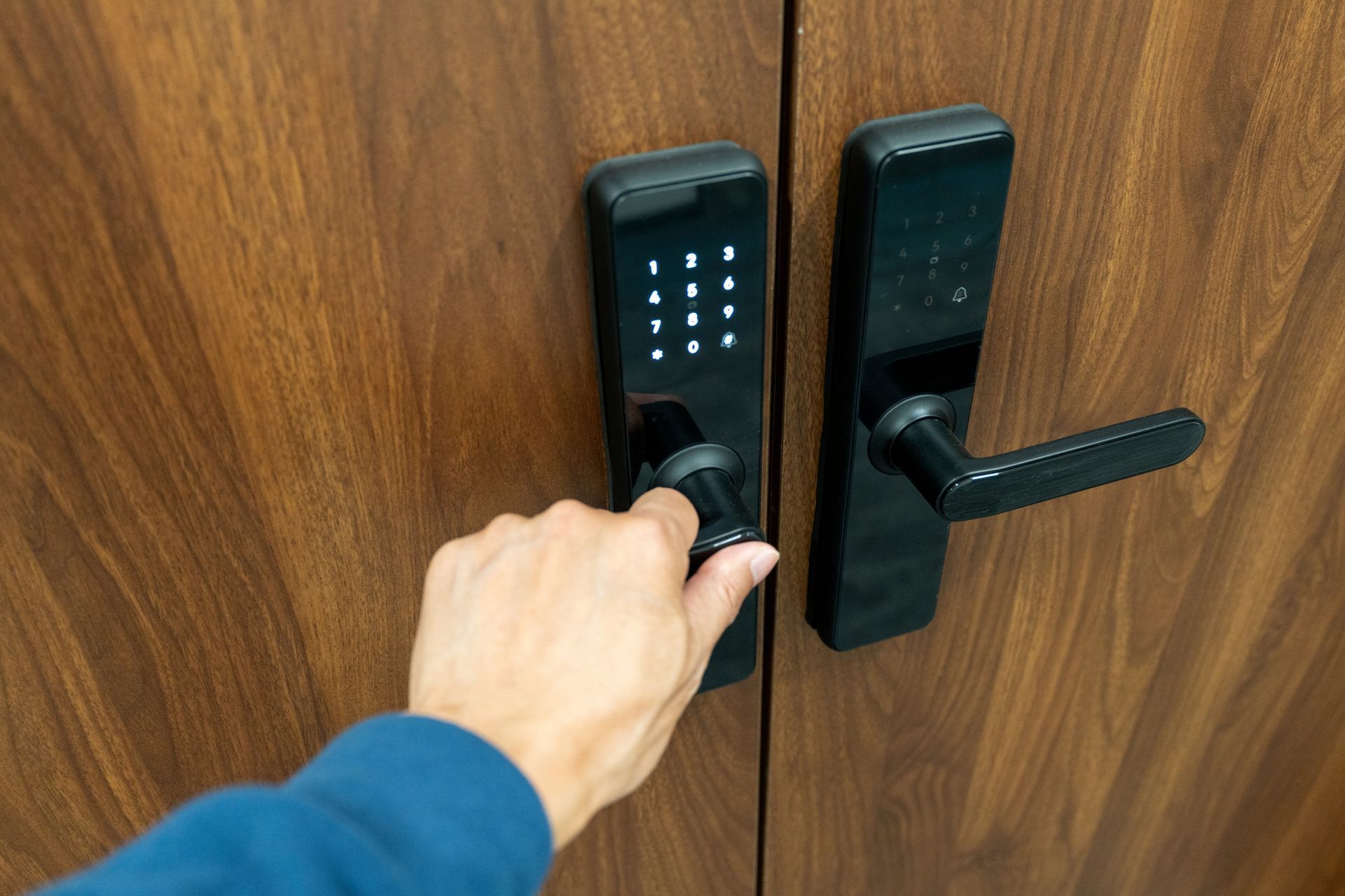 Hand opening a wooden door with a black digital keypad lock and handle.