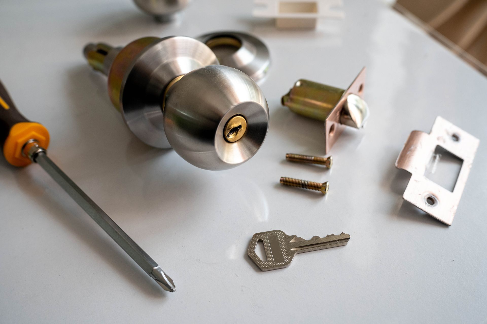 Door lock assembly with screwdriver, key, and screws on a white surface.