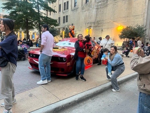 People gather around a red car decorated as Lightning McQueen in an outdoor setting.