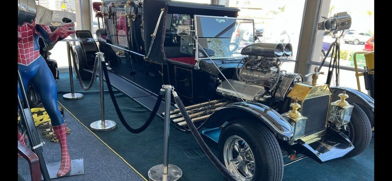 Black hot rod car on display next to a Spider-Man statue.