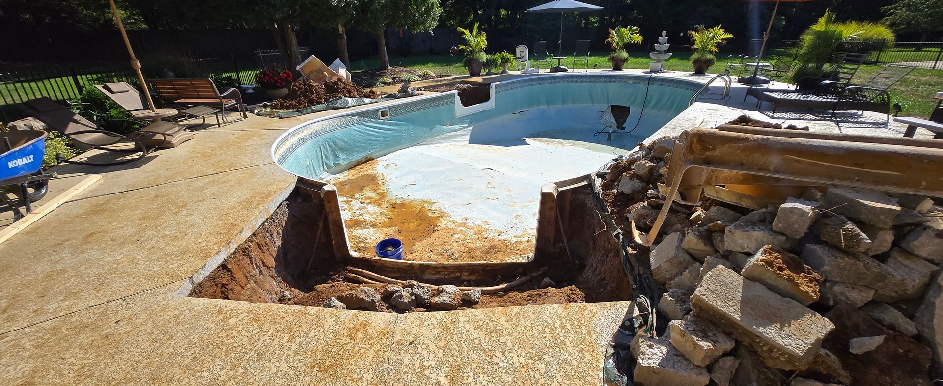 Curved outdoor swimming pool with stone deck and lounge chairs in a sunny landscaped yard