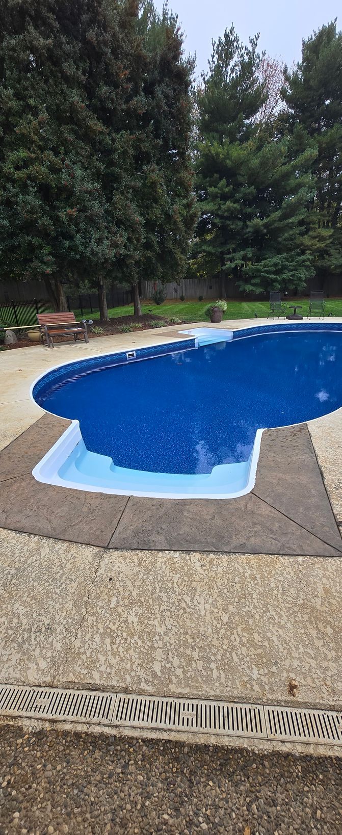 Outdoor swimming pool with blue water beside a textured deck and greenery.