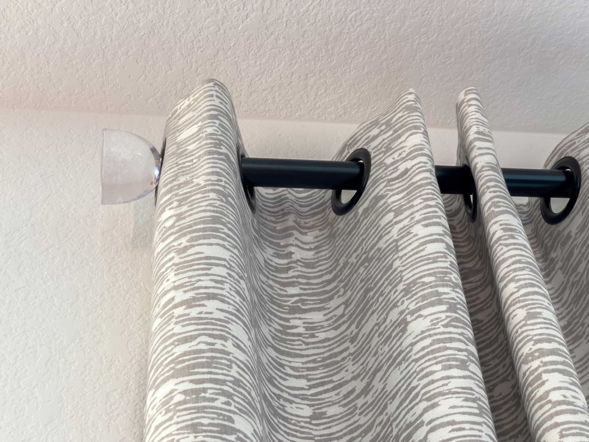 Curtains hanging from a black rod with patterned fabric gathered near the ceiling in a room corner Curtains hanging from a black rod with patterned fabric gathered near the ceiling in a room corner