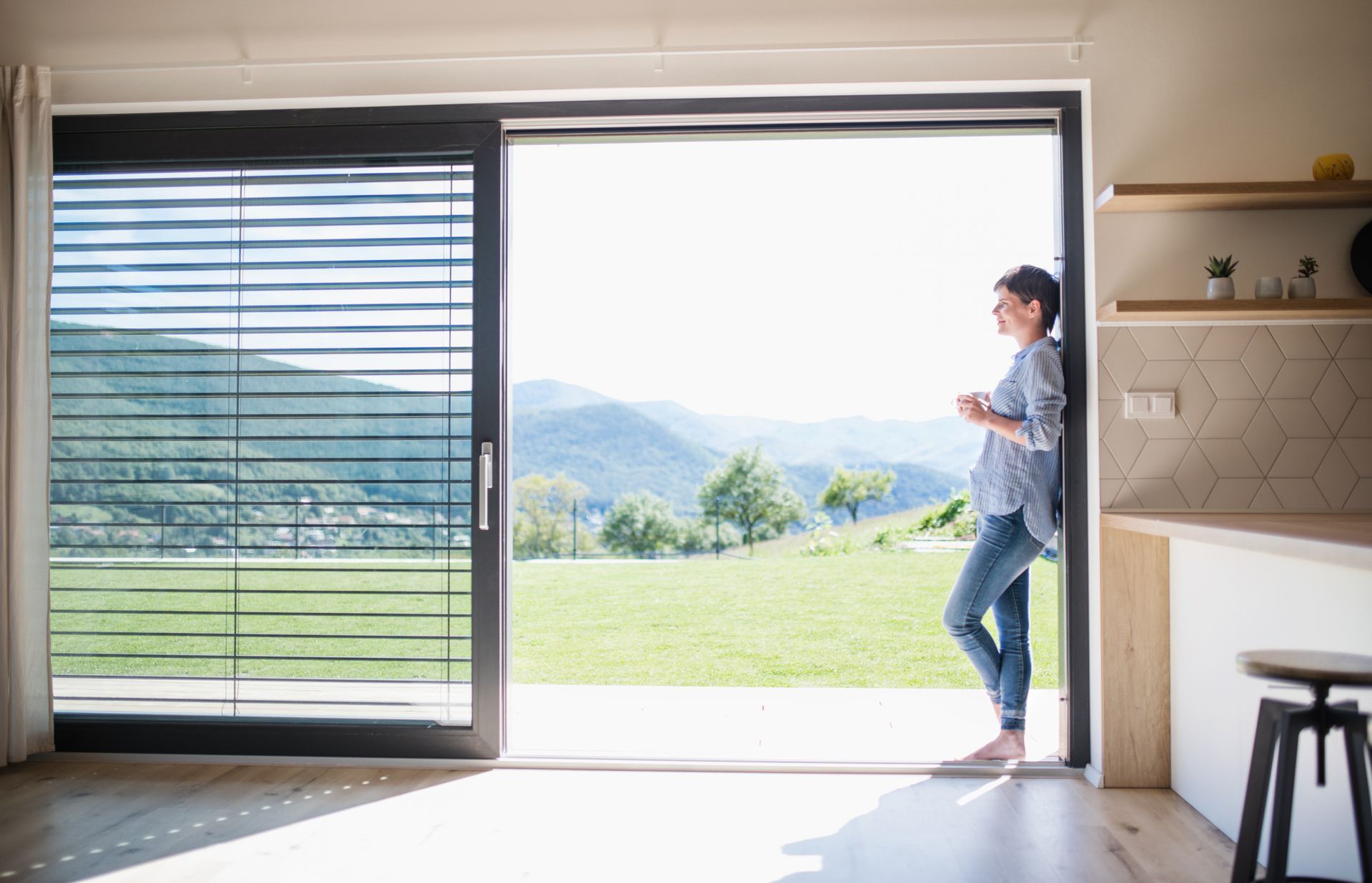A woman is standing in front of a sliding glass door looking out.