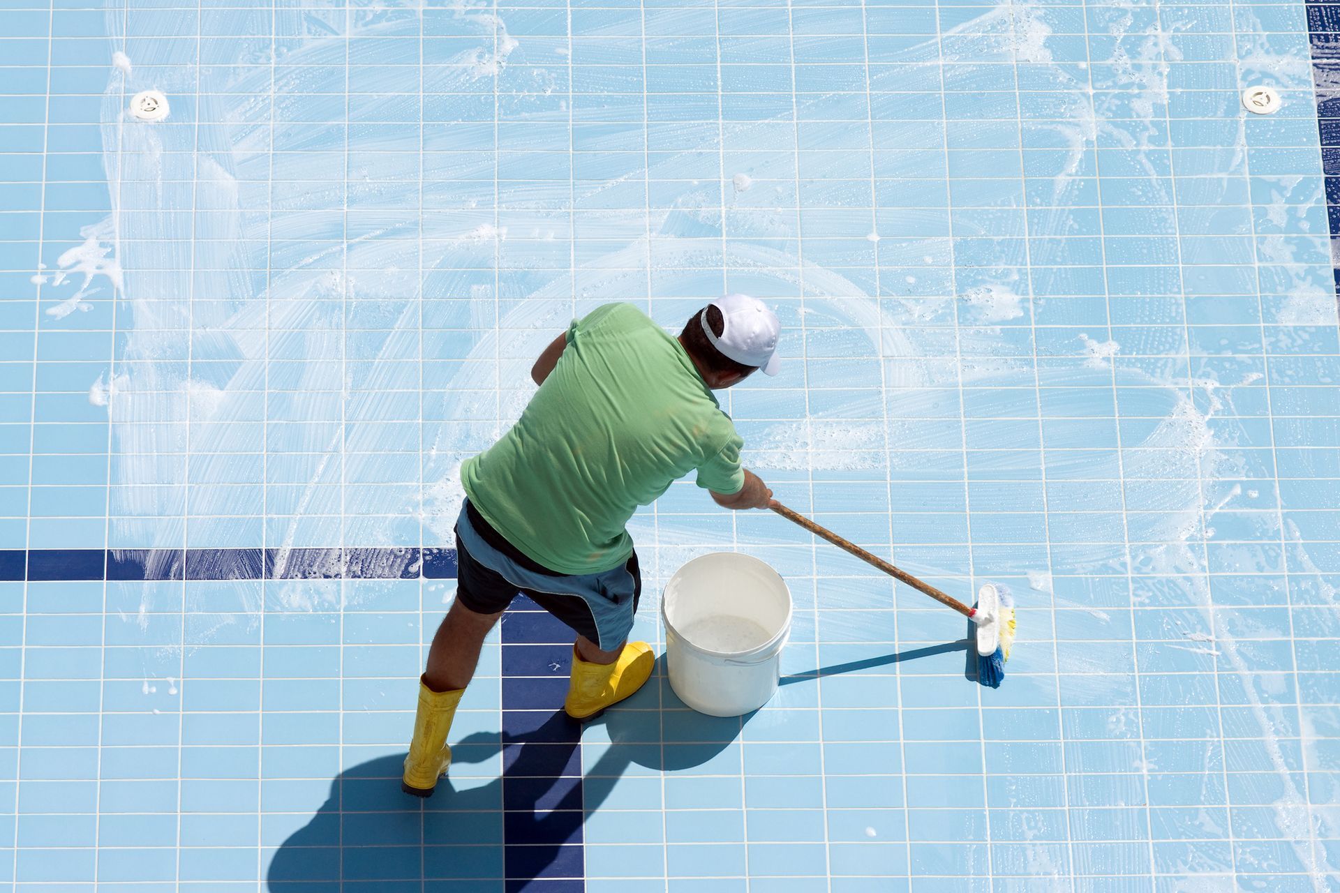 A man is cleaning a swimming pool with a broom and bucket.