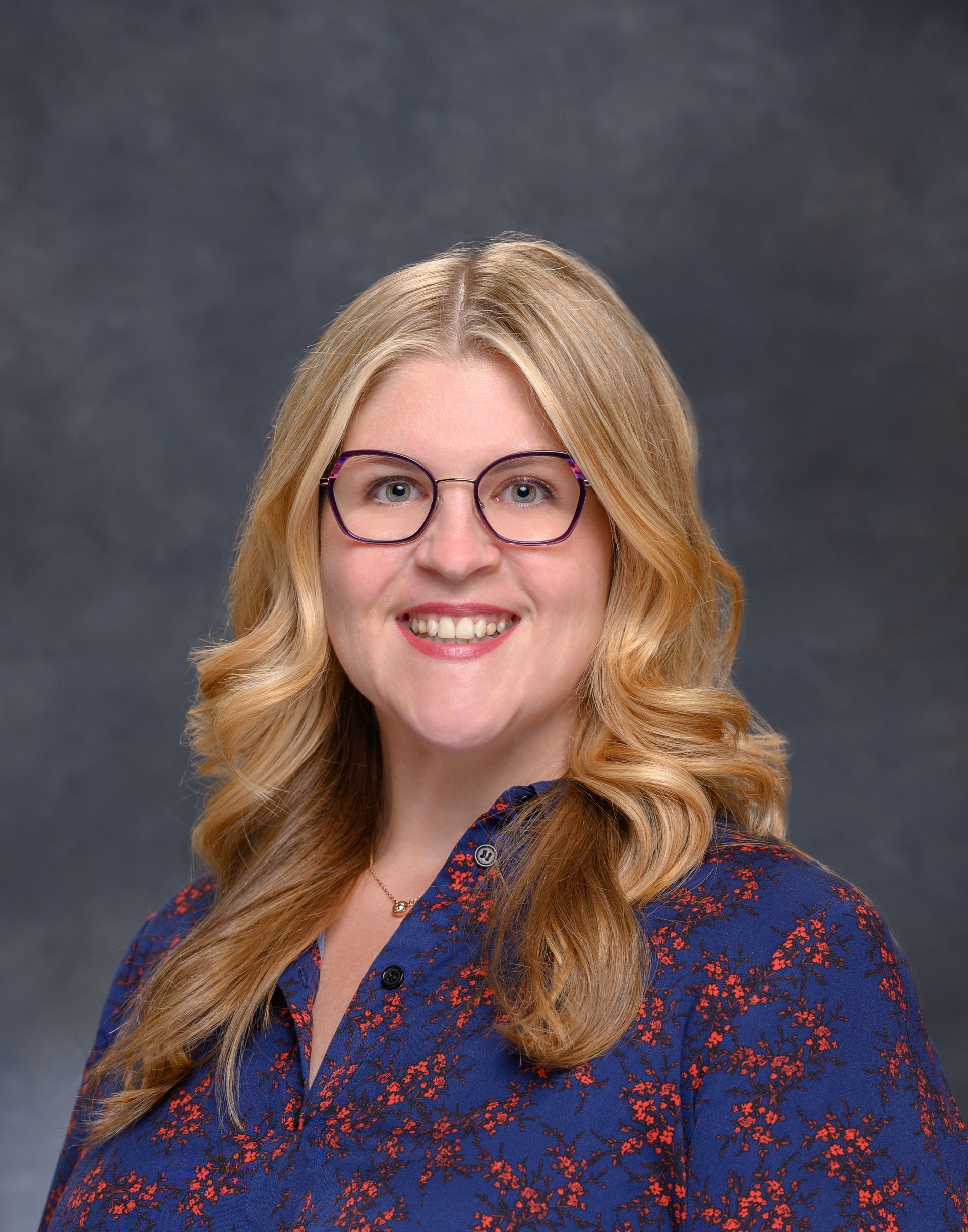 A woman wearing glasses and a blue shirt is smiling for the camera.