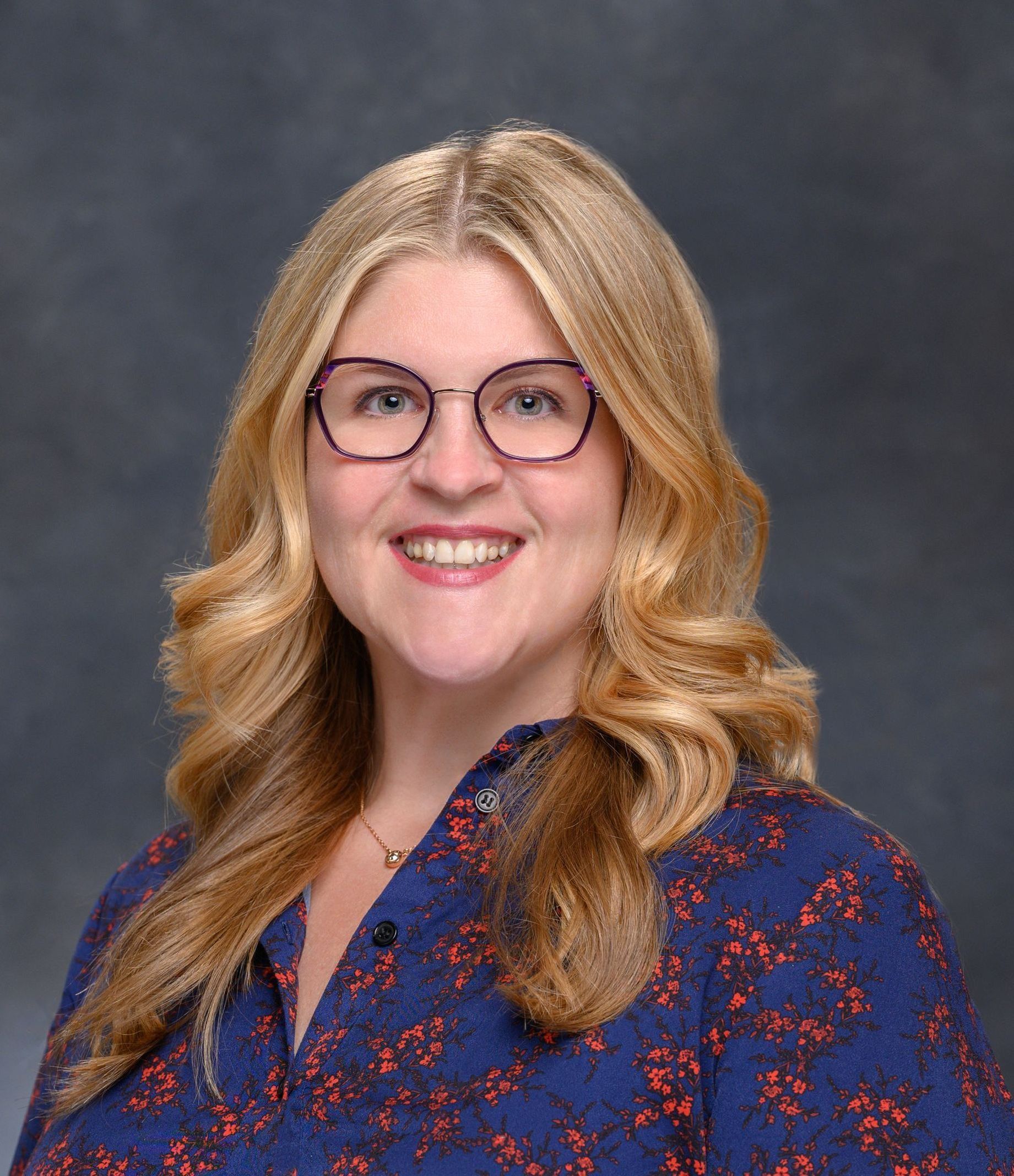 A woman wearing glasses and a blue shirt is smiling for the camera.