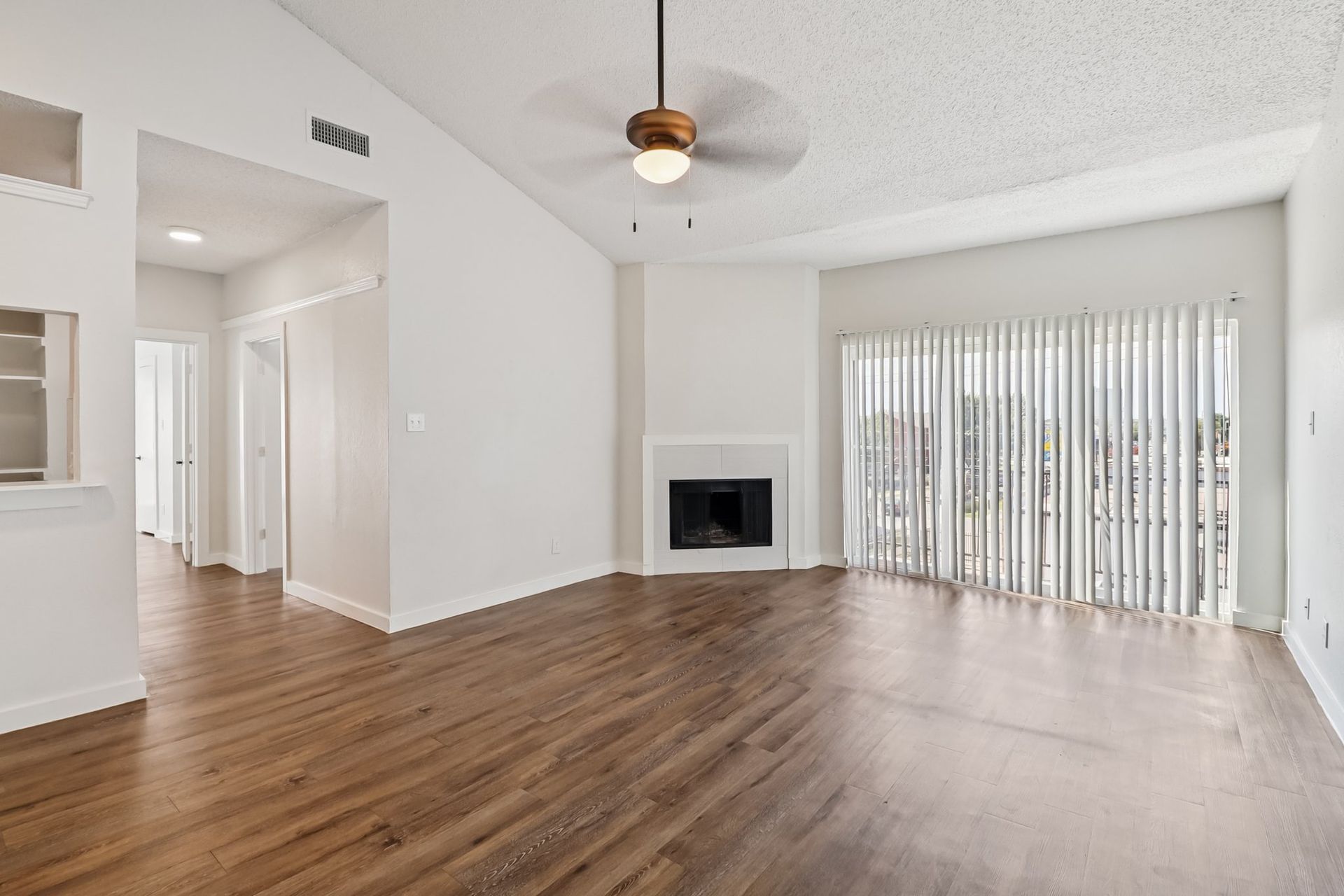 Photo of a living room with plentty of natural lighting and a hallway in the background.
