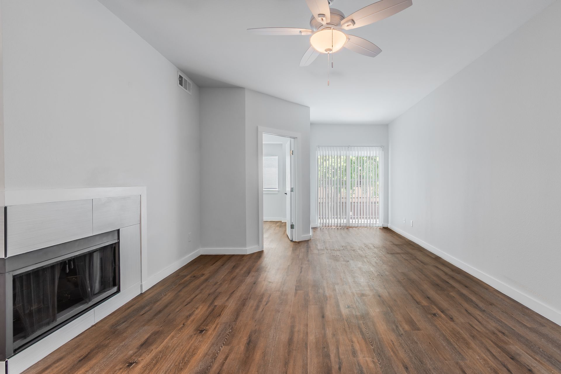 Living room with fireplace, wooden floors, sliding glass door, and ceiling fan.