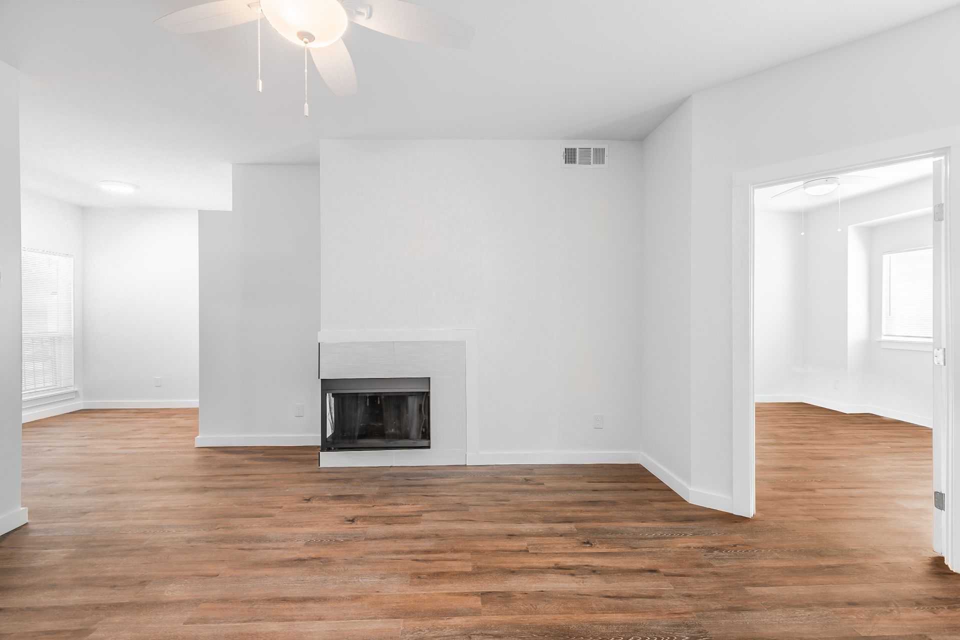 Empty living room with wood floors, white walls, and fireplace.