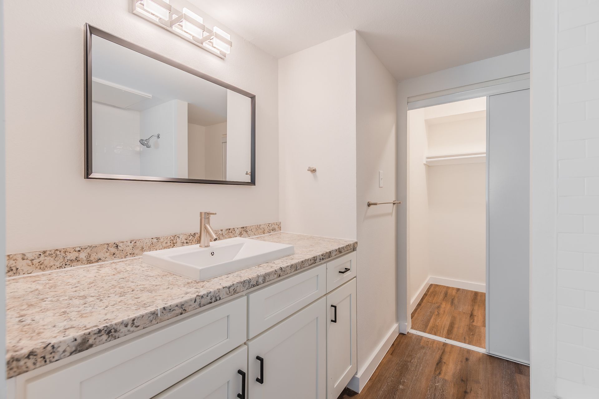 Bathroom with white vanity, granite countertop, rectangular mirror, closet with sliding door.
