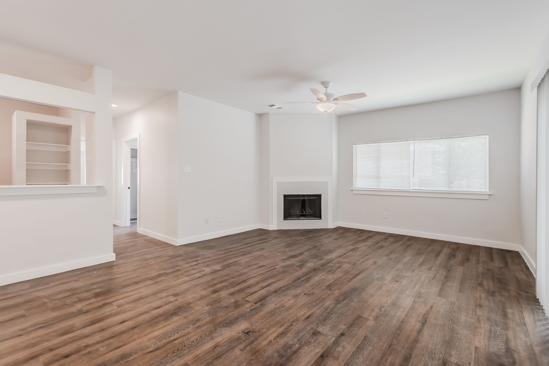Empty living room with dark wood-look floors, fireplace, and white walls.