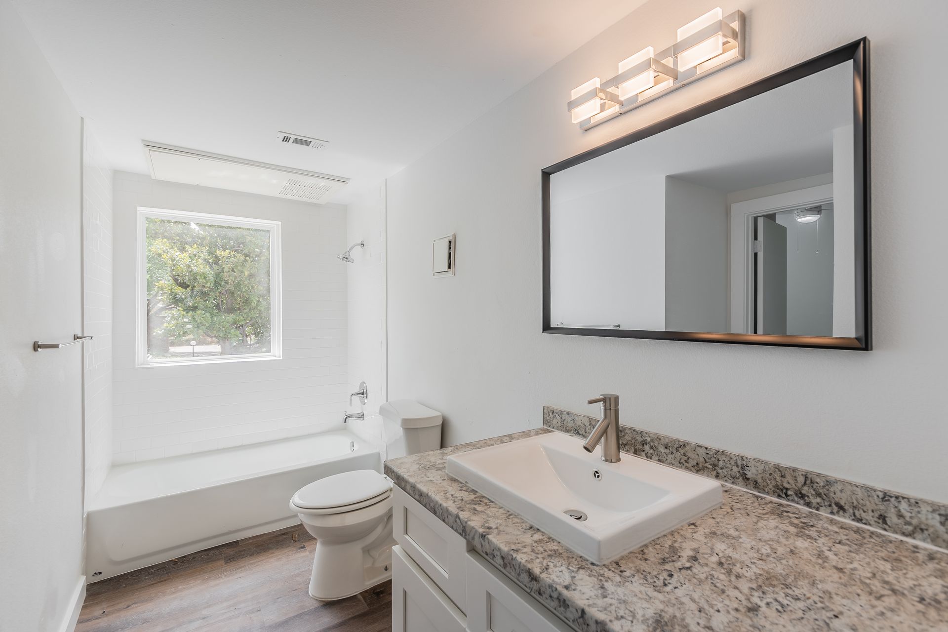 Bright white bathroom with a vanity, mirror, toilet, and a window.