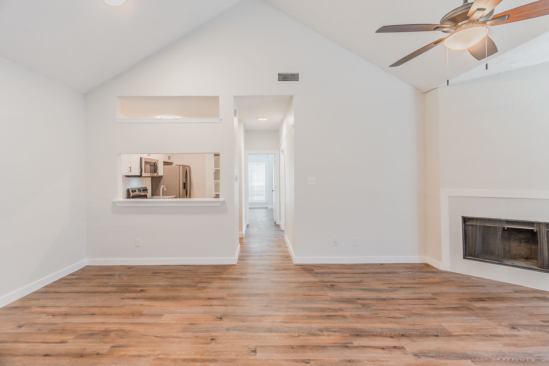 Empty living room with vaulted ceiling, wood flooring, and a fireplace.