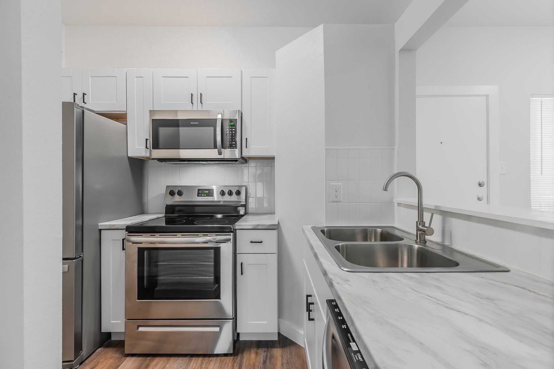 Modern white kitchen with stainless steel appliances and a marble countertop.
