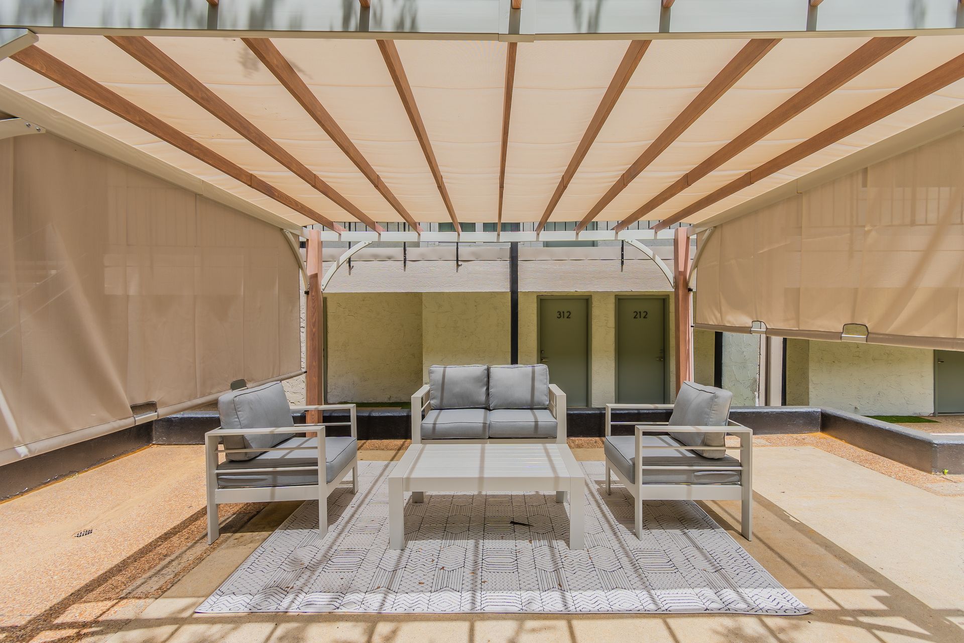 Outdoor seating area with light gray furniture, beneath a beige awning.