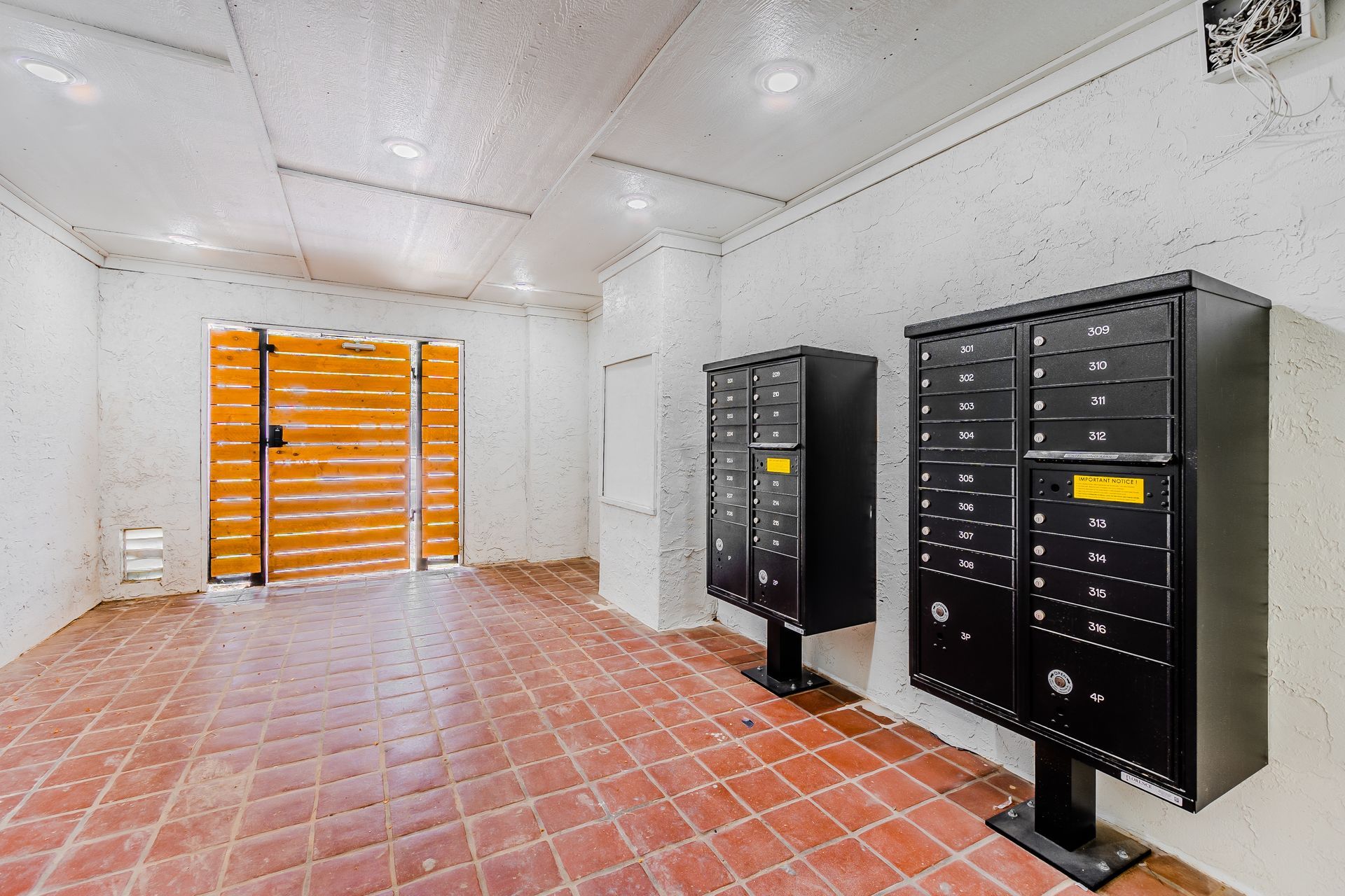 Hallway with red brick floor, mailboxes, and a wooden gate.