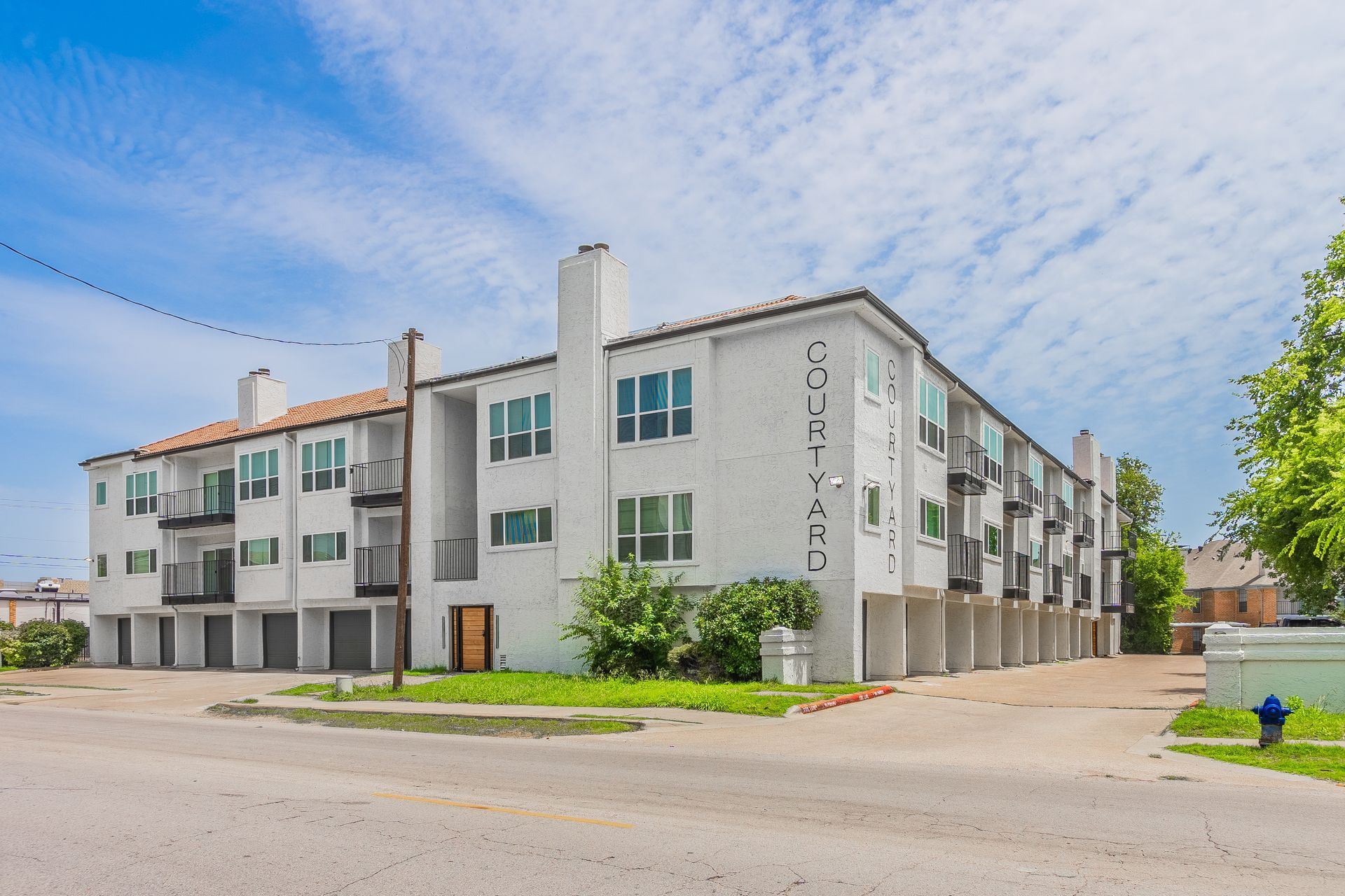 White condo building with balconies, blue sky, and street.