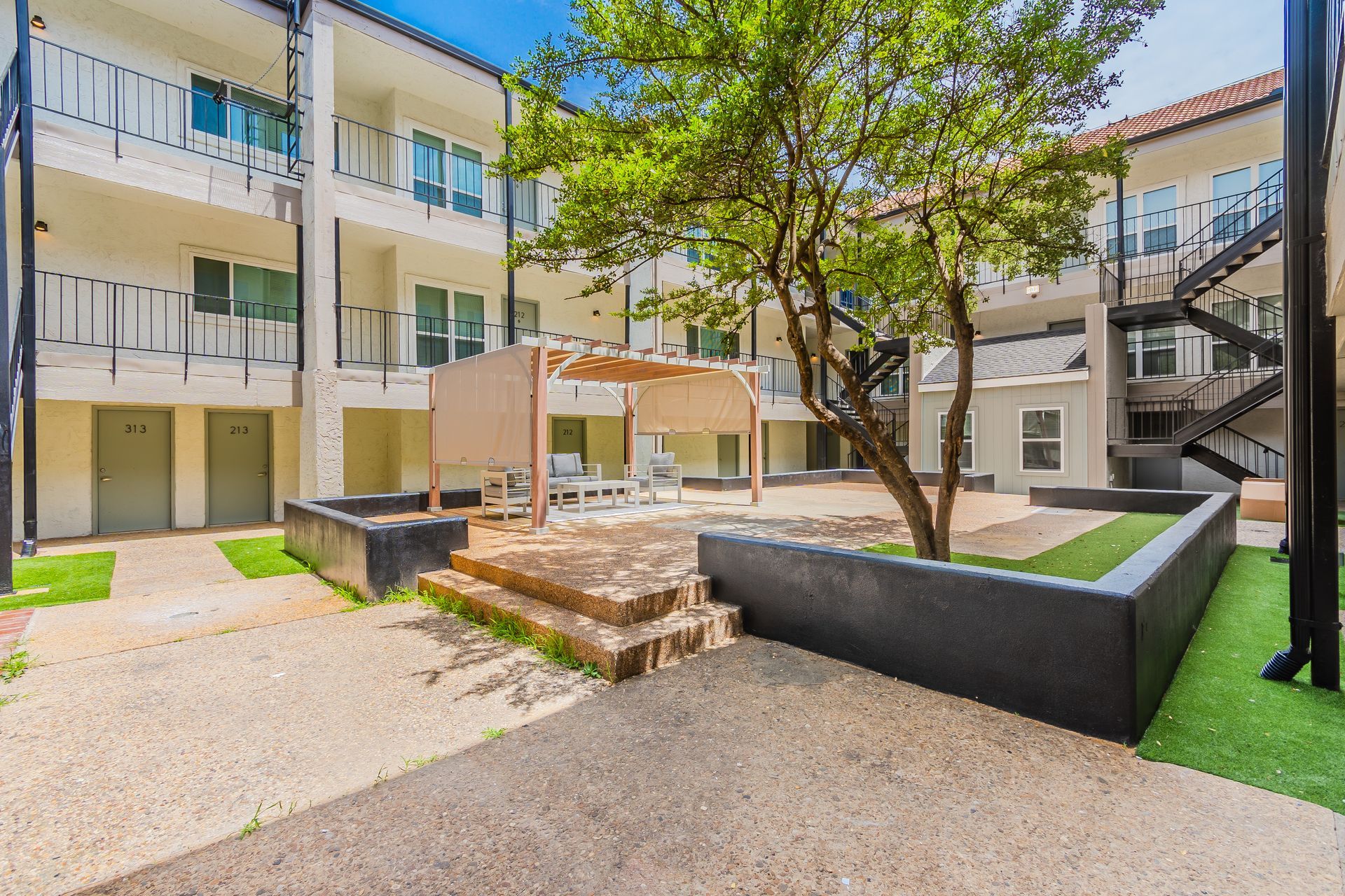 Courtyard with beige buildings, stairs, a gazebo, and a tree.